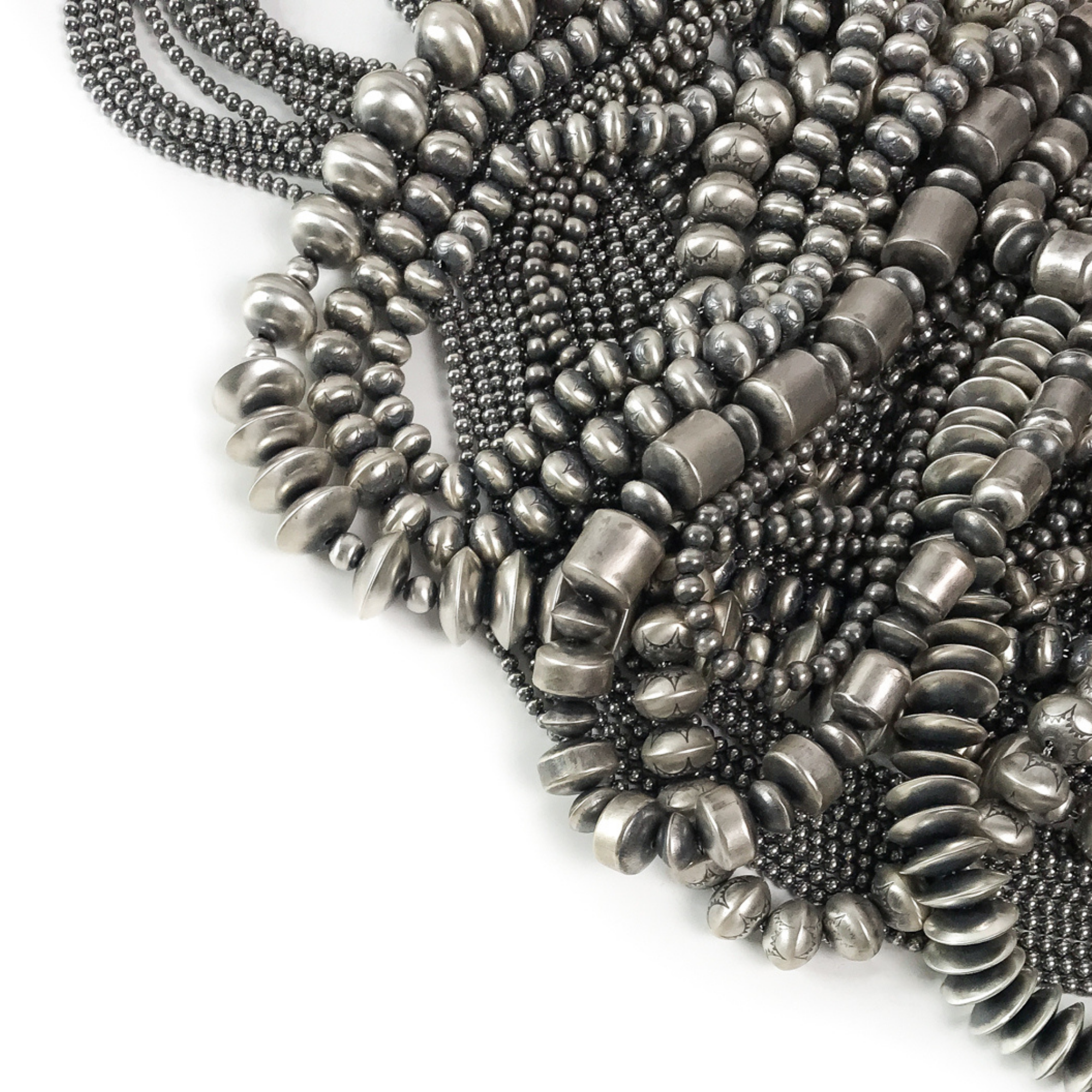 Close-up of a stack of silver beaded necklaces on a white background
