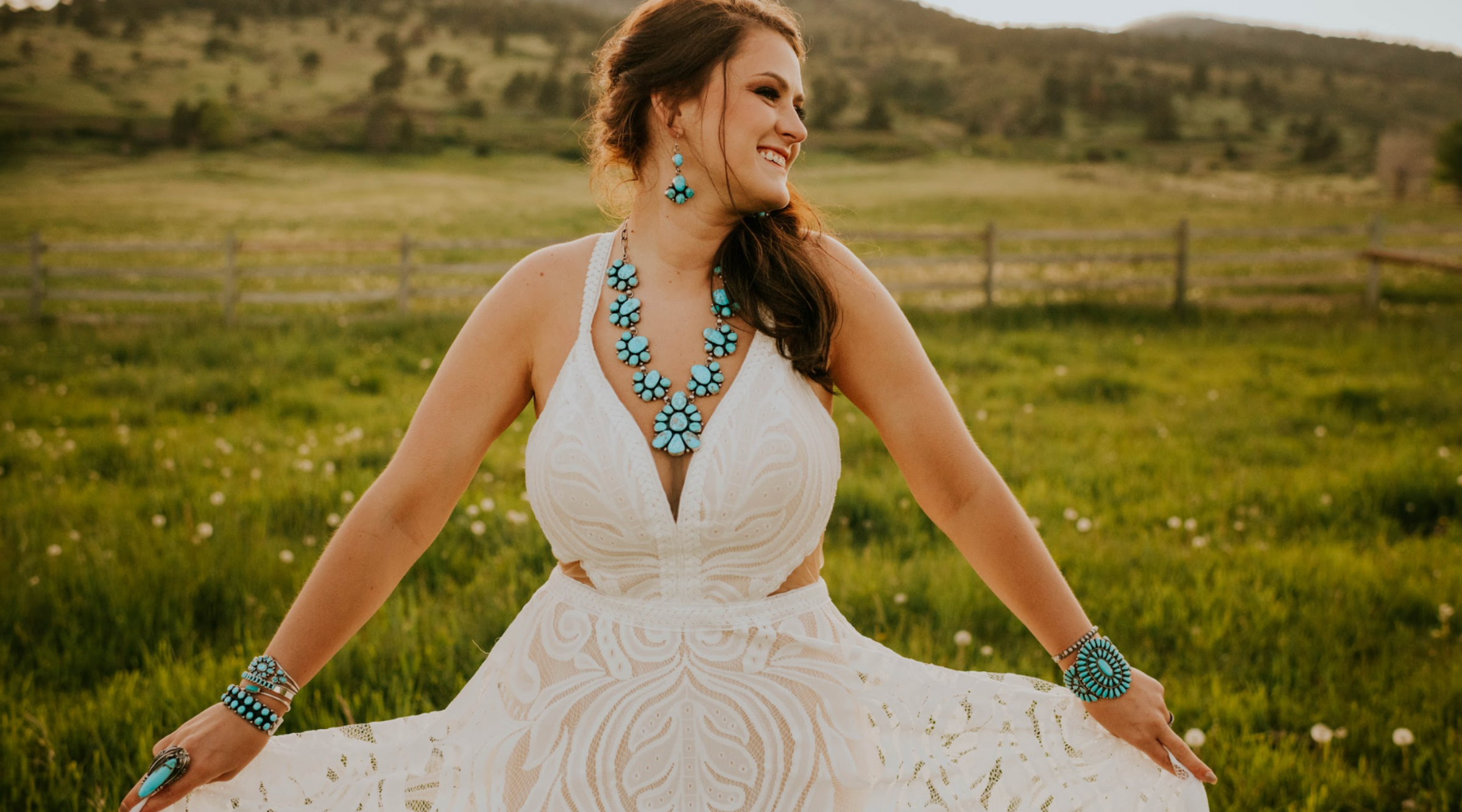 Bride in a lace sleeveless wedding gown wearing turquoise jewelry from Calli Co. Silver. Standing in a green pasture. 