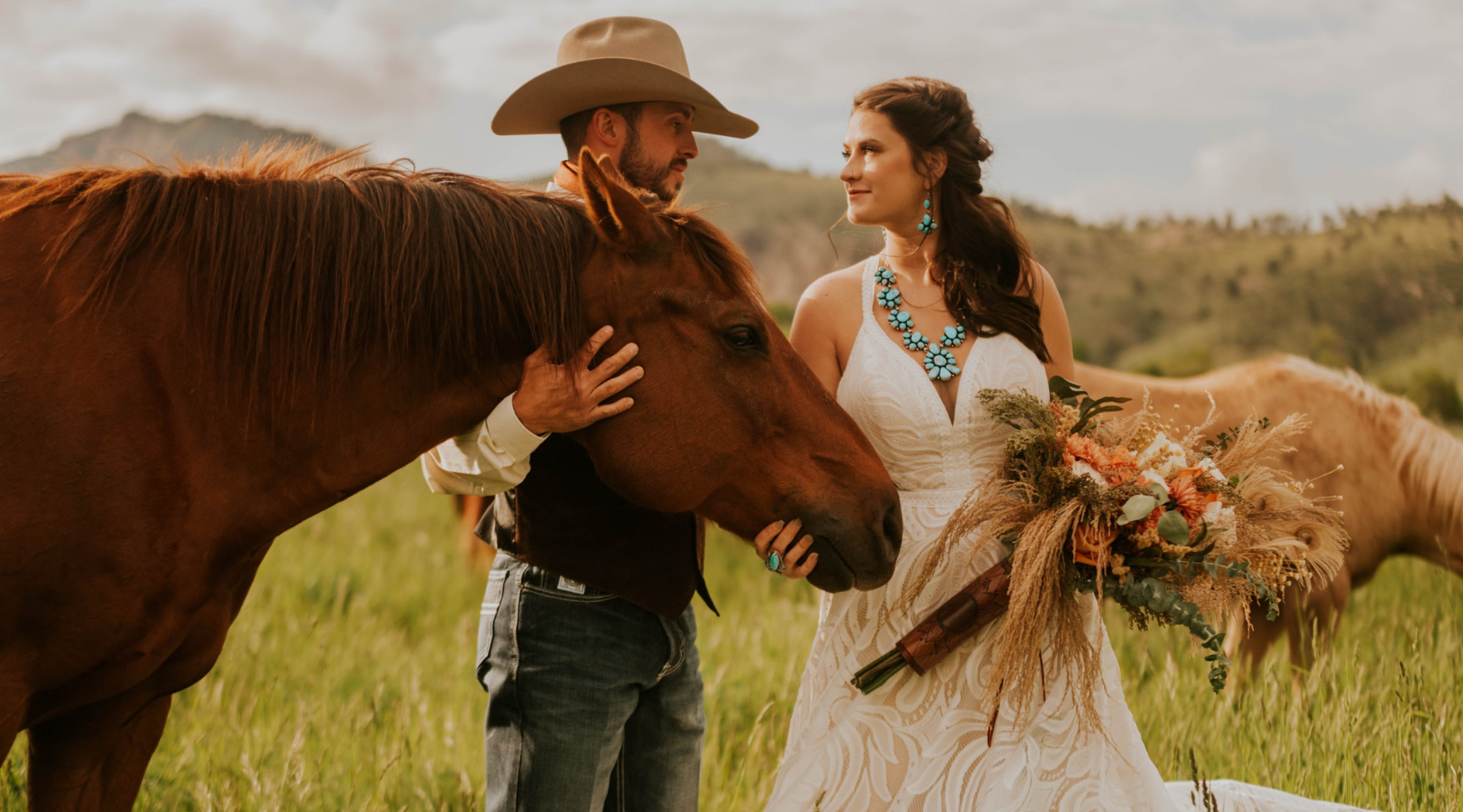 Western bride and groom in a field with horses amongst mountains. Bride is wearing turquoise and silver jewelry from Calli Co. Silver. 