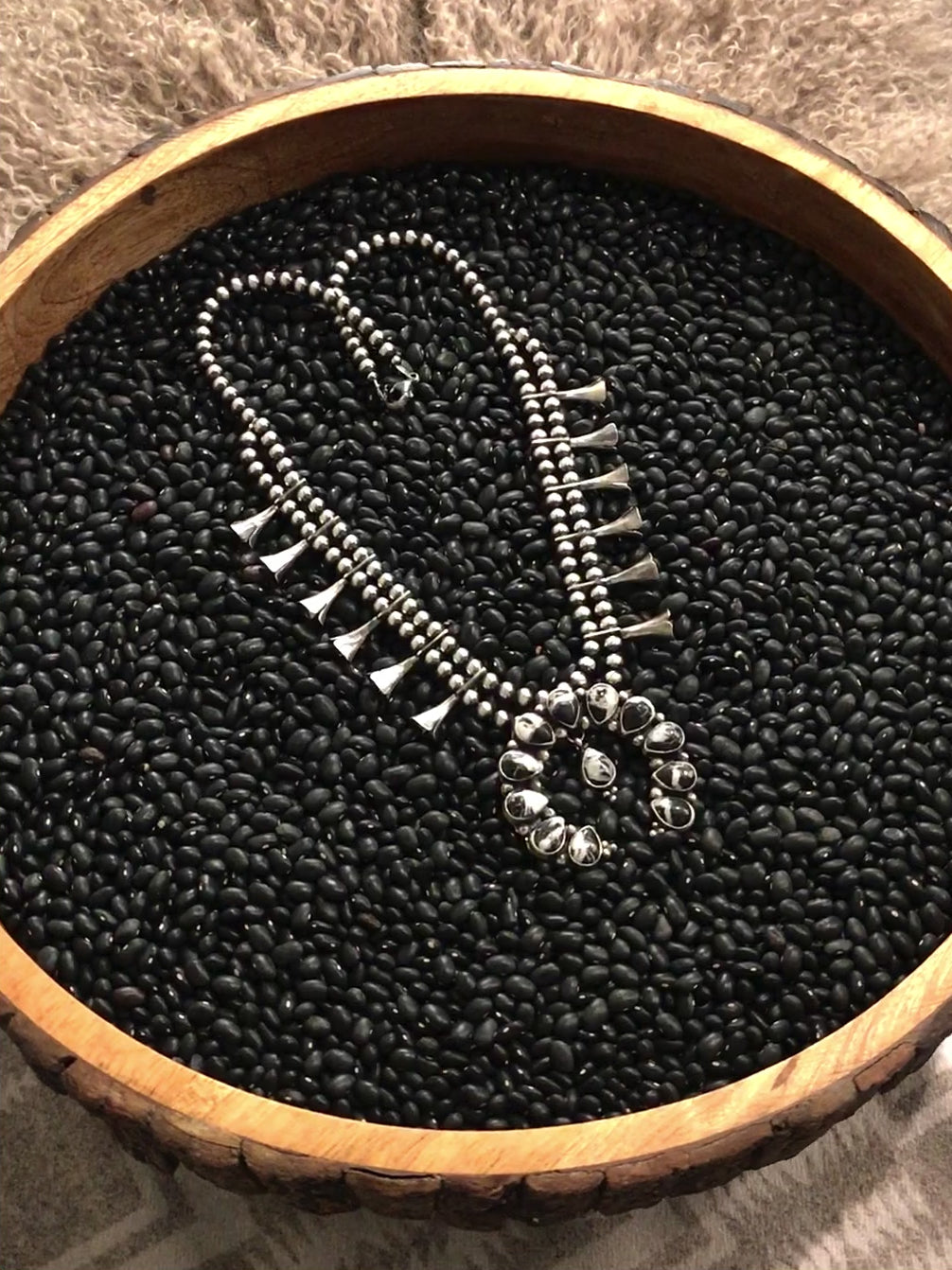 The Monarch Squash Blossom Necklace Set from Calli Co Silver. Displayed on a black textured backdrop rotating on a display in a circle. Squash blossom necklace with white buffalo stones and sterling silver pearl beads and drop accents. Shown with coordinating dangle earrings.  