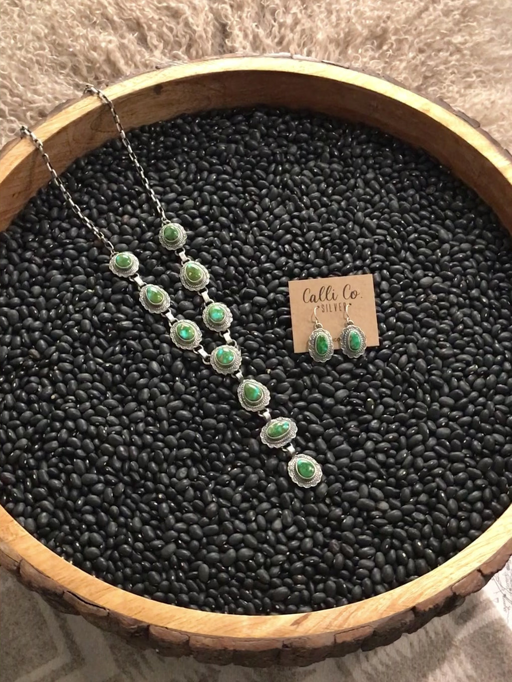 The Bonville lariat Necklace Set from Calli Co Silver. Displayed on a black textured backdrop rotating on a display in a circle.
Sterling silver and Sonoran Gold turquoise
Rope trim accents
Hand-stamped details
Adjustable link chain 
22" total length plus 4" lariat drop 
Includes matching earrings that measure 1 1/4" long
Stamped sterling and signed by Navajo artist 
Colors: Green and blue