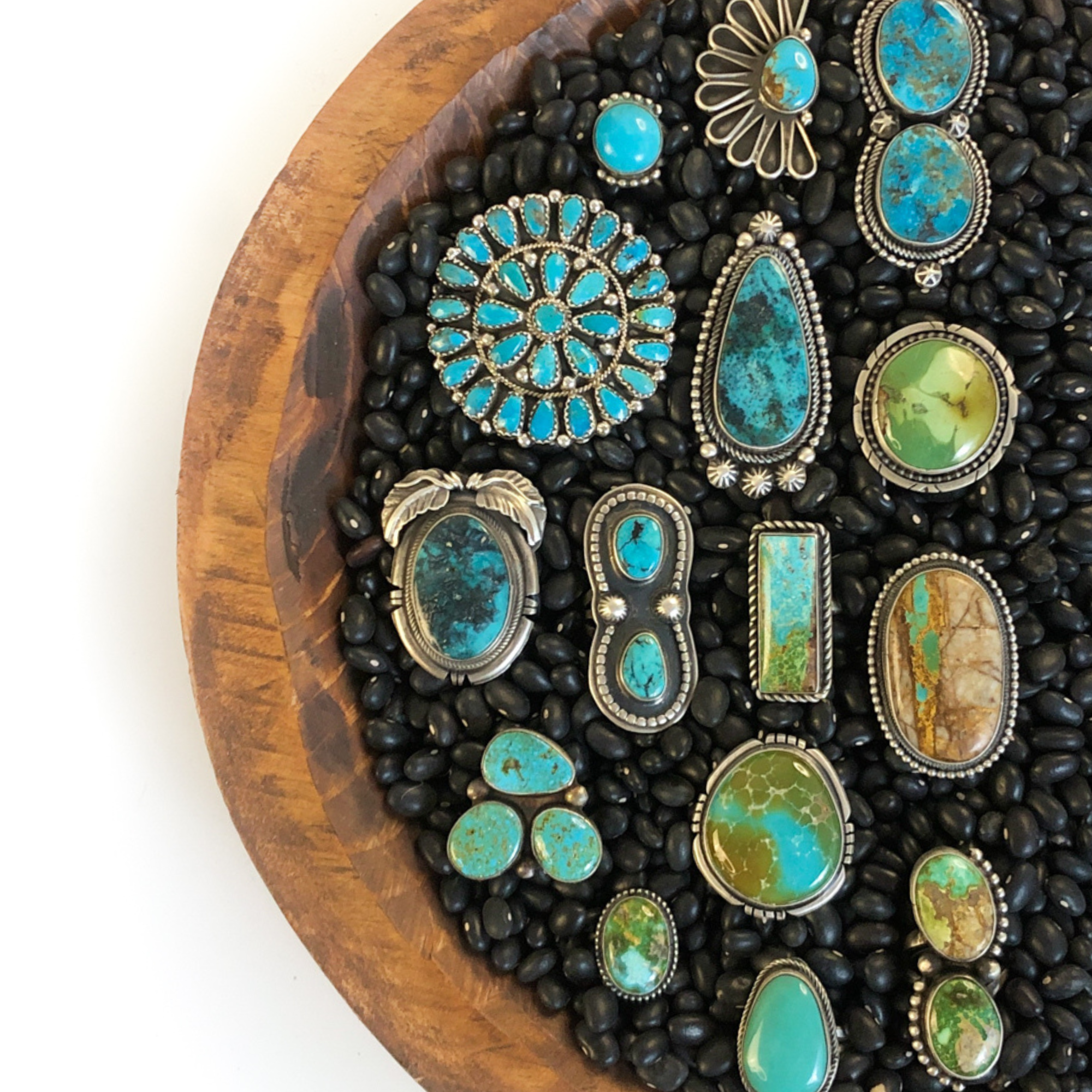 Collection of turquoise and green gemstone rings on a wooden board with black stones.